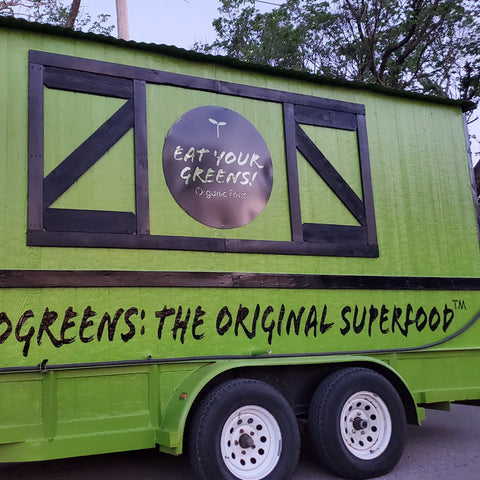 Green and black trailer with Eat Your Greens organic farm logo and text saying Microgreens The Original Superfood