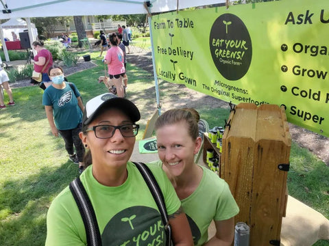 Full photo of founders of Eat Your Greens Organic Farm April and Christa Zuniga at farmers market