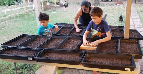 Two children and Christa Zuniga planting microgreens outdoors